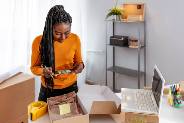 Young start up small business African-American owner packing cardboard box at workplace. Freelance woman seller prepare parcel box of product for deliver to customer. Online selling, e-commerce, shipping concept